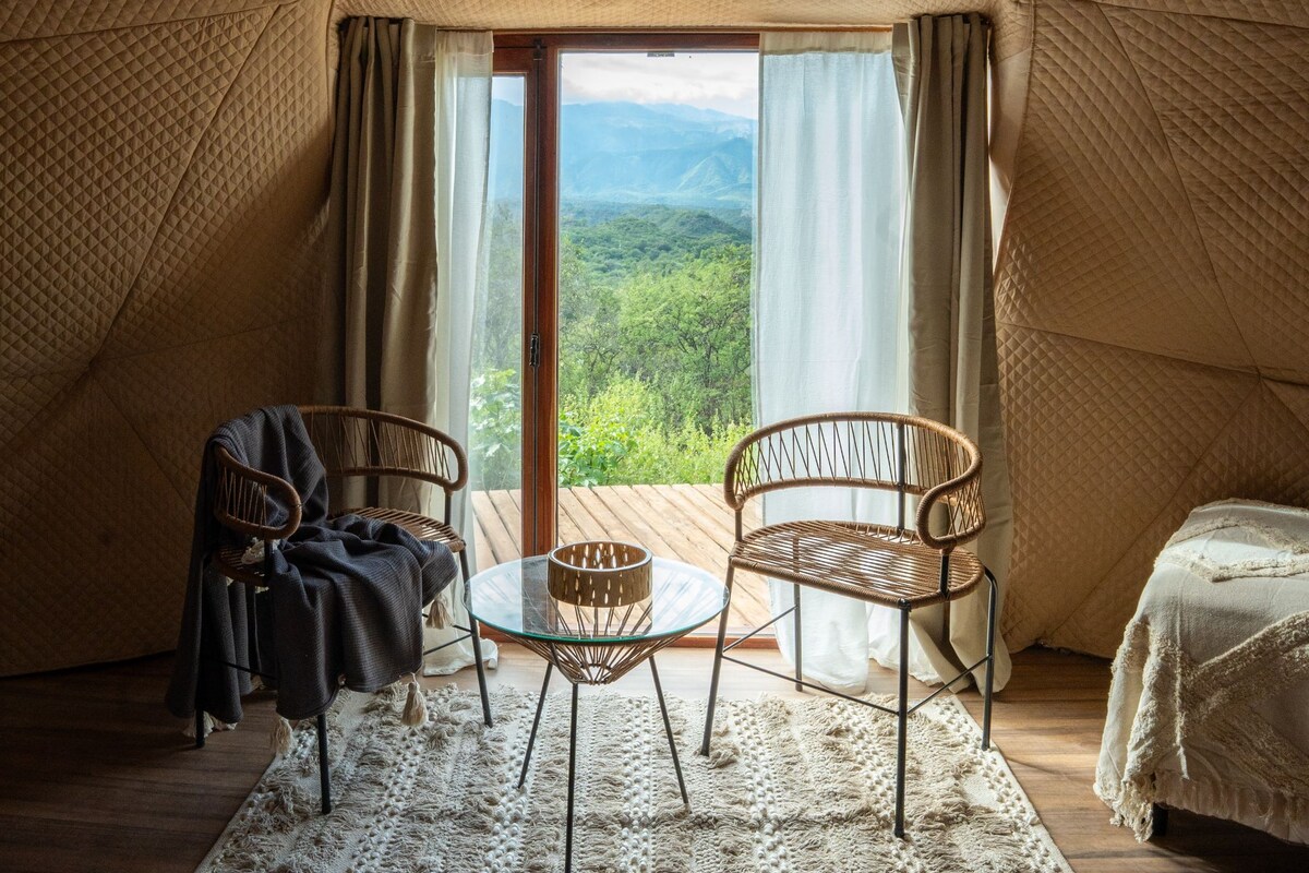 A cozy room with a large window, two wicker chairs, a small glass table, and a bed.