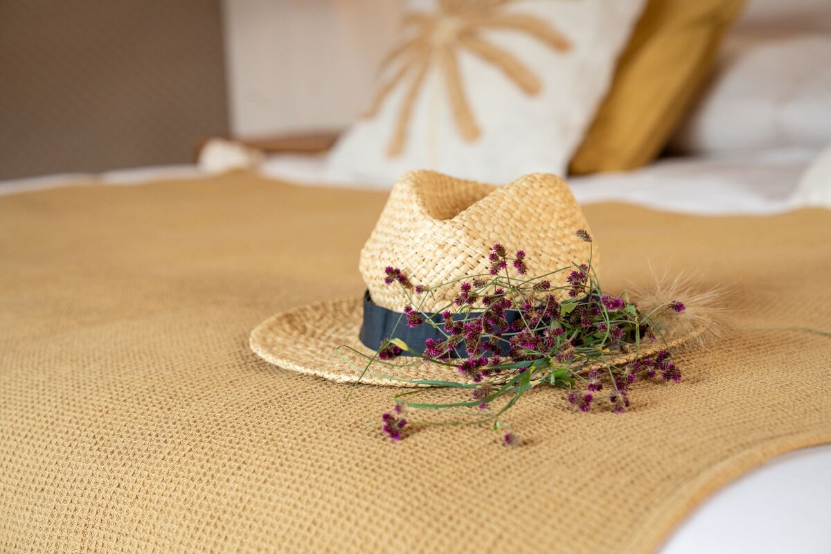 A straw hat with purple flowers on a textured fabric surface.