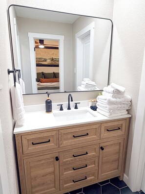 A bathroom with a large mirror, a white sink, a wooden vanity with drawers, and a stack of white towels. - Modern Farmhouse Design, Texas Charm! (Keller)