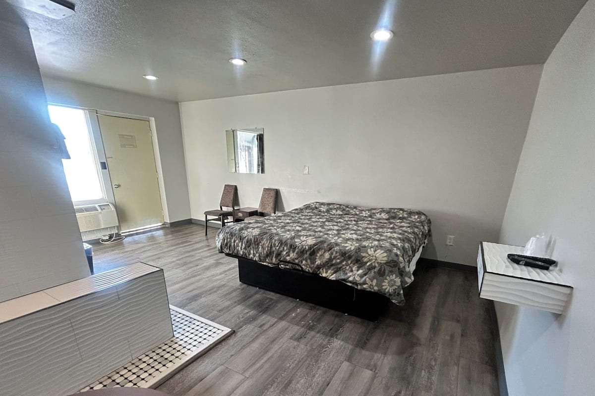 A bedroom with a bed, a chair, a desk, and a mirror.
