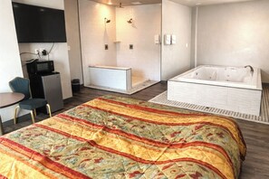Ein Hotelzimmer mit Bett, Schreibtisch, Mikrowelle, Kühlschrank, Duschbereich und Badewanne.