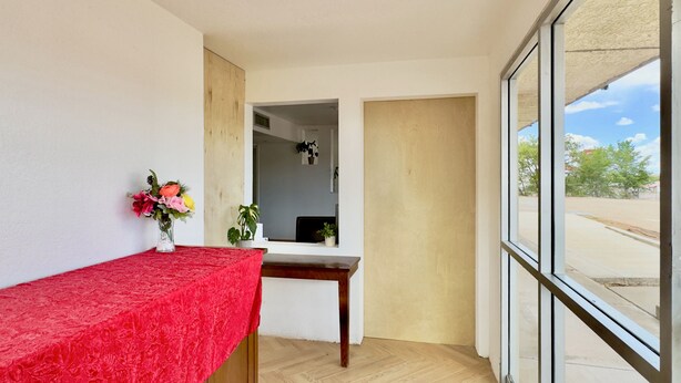 A room with a wooden desk, a red tablecloth, a vase with flowers, and a view through a large window. - Signature Inn Socorro (Socorro)