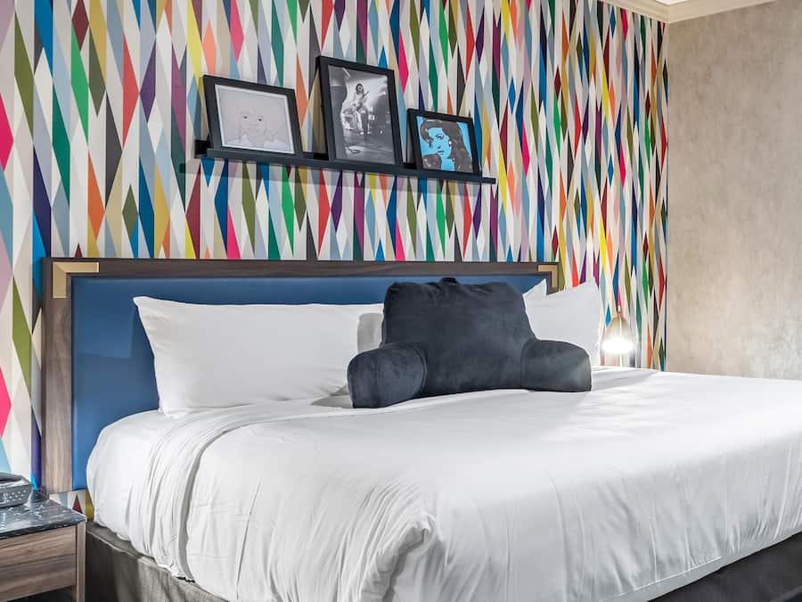 Habitación de hotel con cama, mesita de noche, pared con patrones geométricos de colores y cuadros enmarcados.
