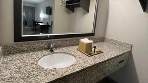 A bathroom with a granite countertop, a white sink, a mirror, and a towel dispenser. - Signature Inn Socorro (Socorro)