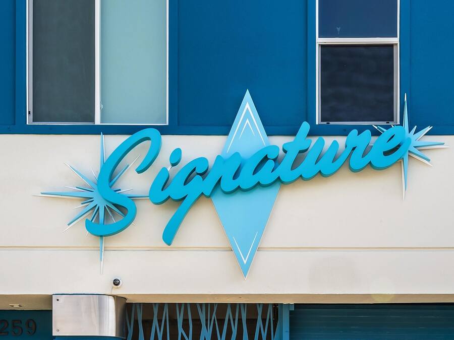 Um edifício com uma placa que diz 'Signature' numa fonte estilizada.