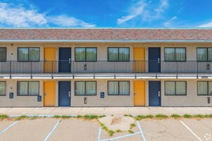 A multi-story hotel with a flat roof, balconies, and a parking lot with marked spaces.