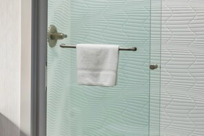 Un baño con pared texturizada, una toalla colgada en un perchero metálico y una puerta con picaporte metálico.