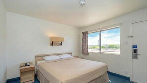 A hotel room with a single bed, a bedside table with a phone, a window with curtains, and a door with a lock. - Signature Inn Socorro (Socorro)