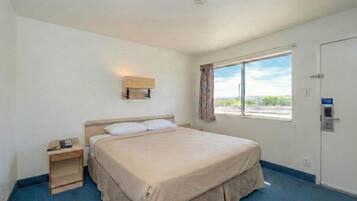 Une chambre d’hôtel avec un lit simple, une table de chevet avec un téléphone, une fenêtre avec des rideaux et une porte avec une serrure.
