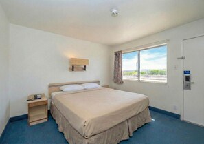 A hotel room with a single bed, a bedside table with a phone, a window with curtains, and a door with a lock. - Signature Inn Socorro (Socorro)