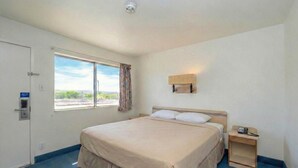 A hotel room with a large bed, a bedside table with a lamp, a window with a view, and a door with a lock. - Signature Inn Socorro (Socorro)