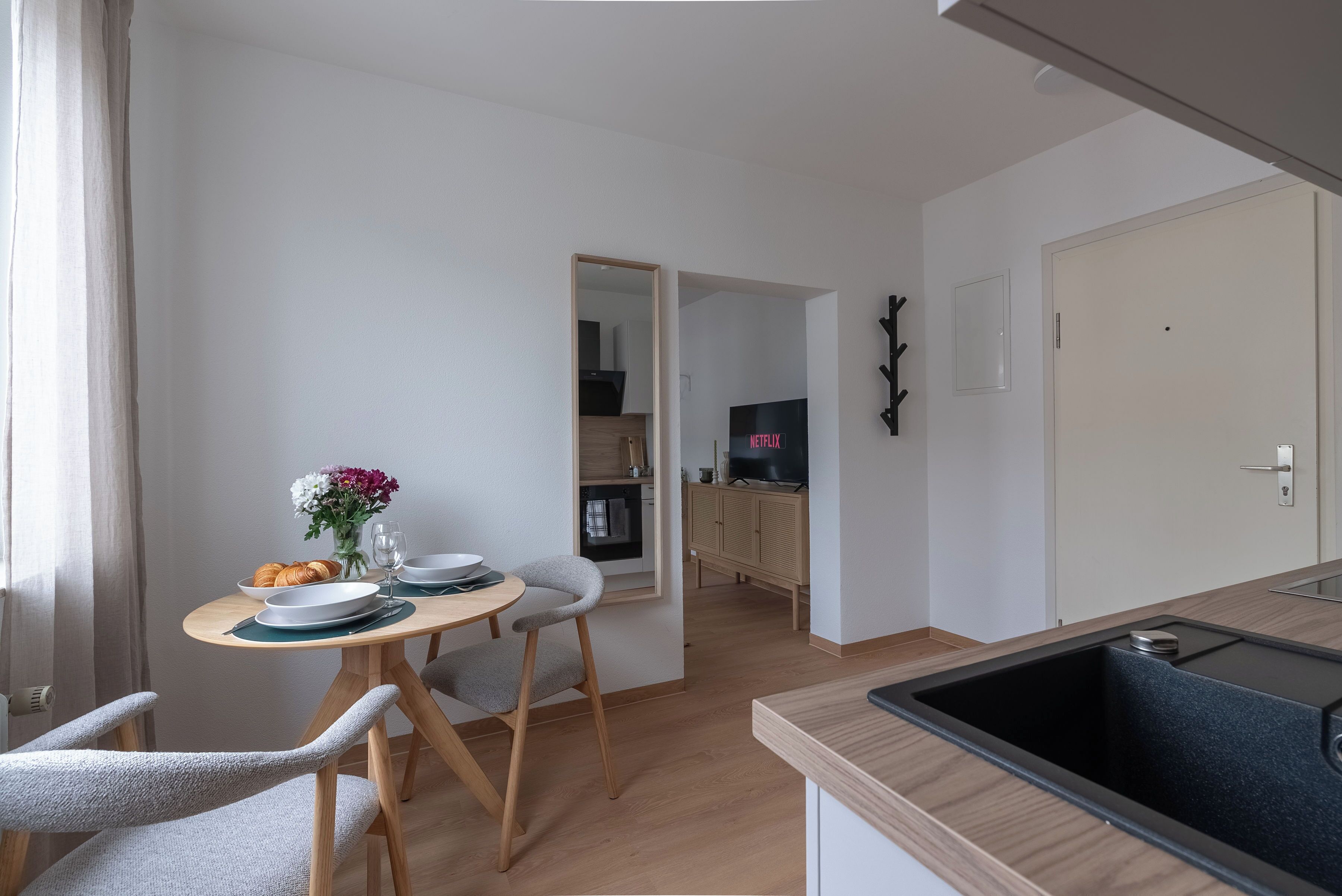 Een moderne keuken met een zwarte spoelbak, houten kastjes en een eethoek met een tafel gedekt voor twee personen.