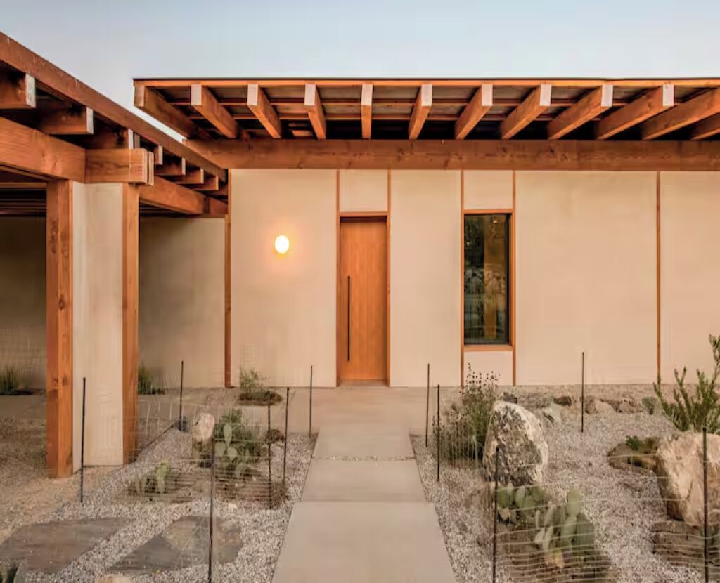 A modern building with a wooden pergola, a central door, and a pathway leading to it.