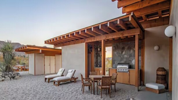 Um pátio moderno ao ar livre, com piso de pedra, pérgola de madeira e área de churrasco.