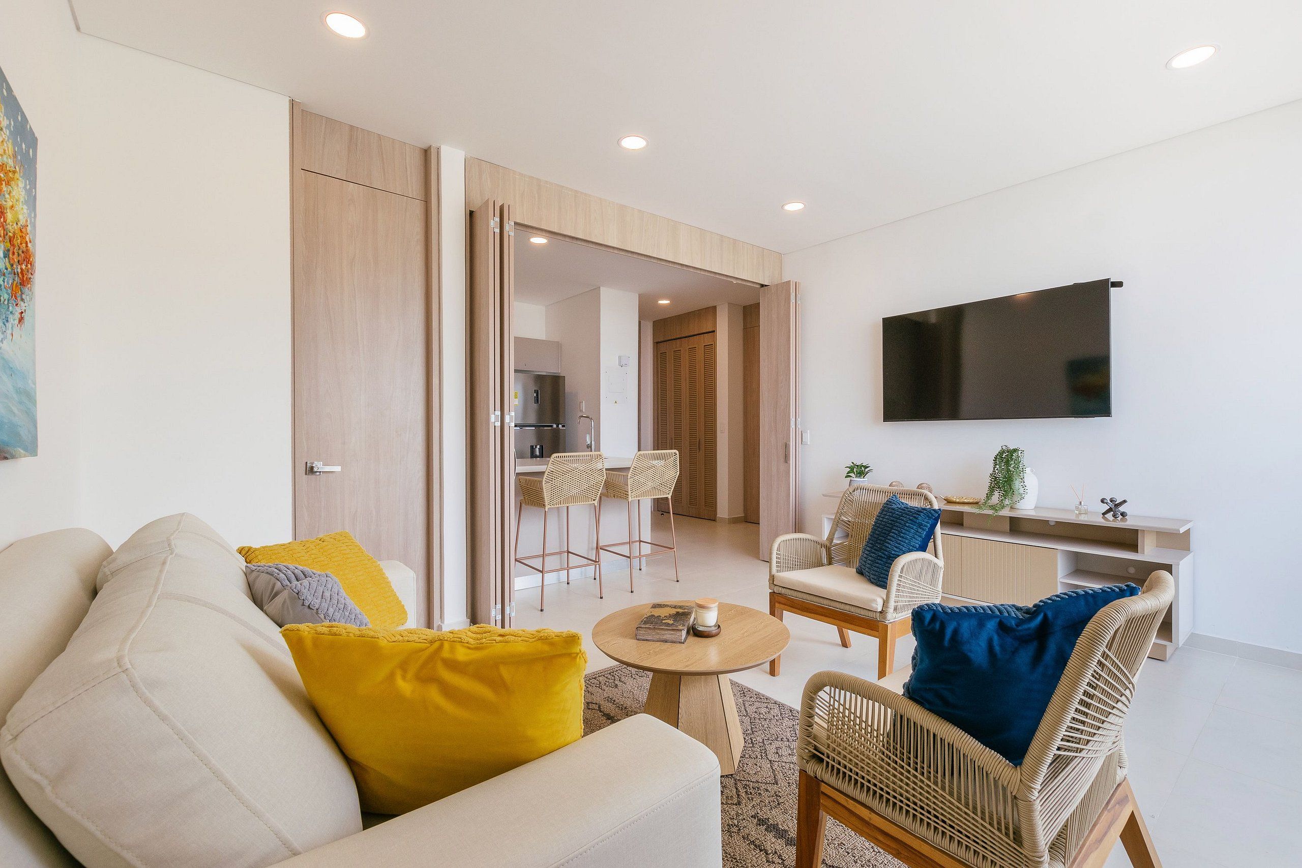 Un salon moderne avec un canapé, des fauteuils, une table basse et un téléviseur fixé au mur.