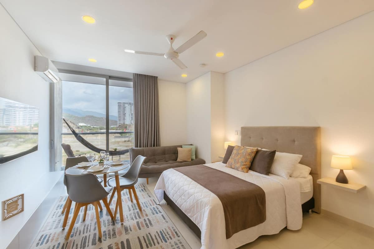 Une chambre d’hôtel moderne équipée d’un lit, d’une table à manger avec des chaises, d’un canapé, d’un ventilateur de plafond et offrant une vue sur la ville.