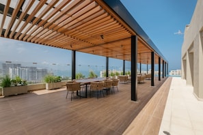Une terrasse sur le toit agrémentée d’une pergola en bois, d’une table à manger avec des chaises, de plantes en pot et offrant une vue sur la ville.