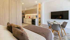 Ein modernes Hotelzimmer mit Bett, Essbereich, Küchenzeile und Wand-Fernseher.