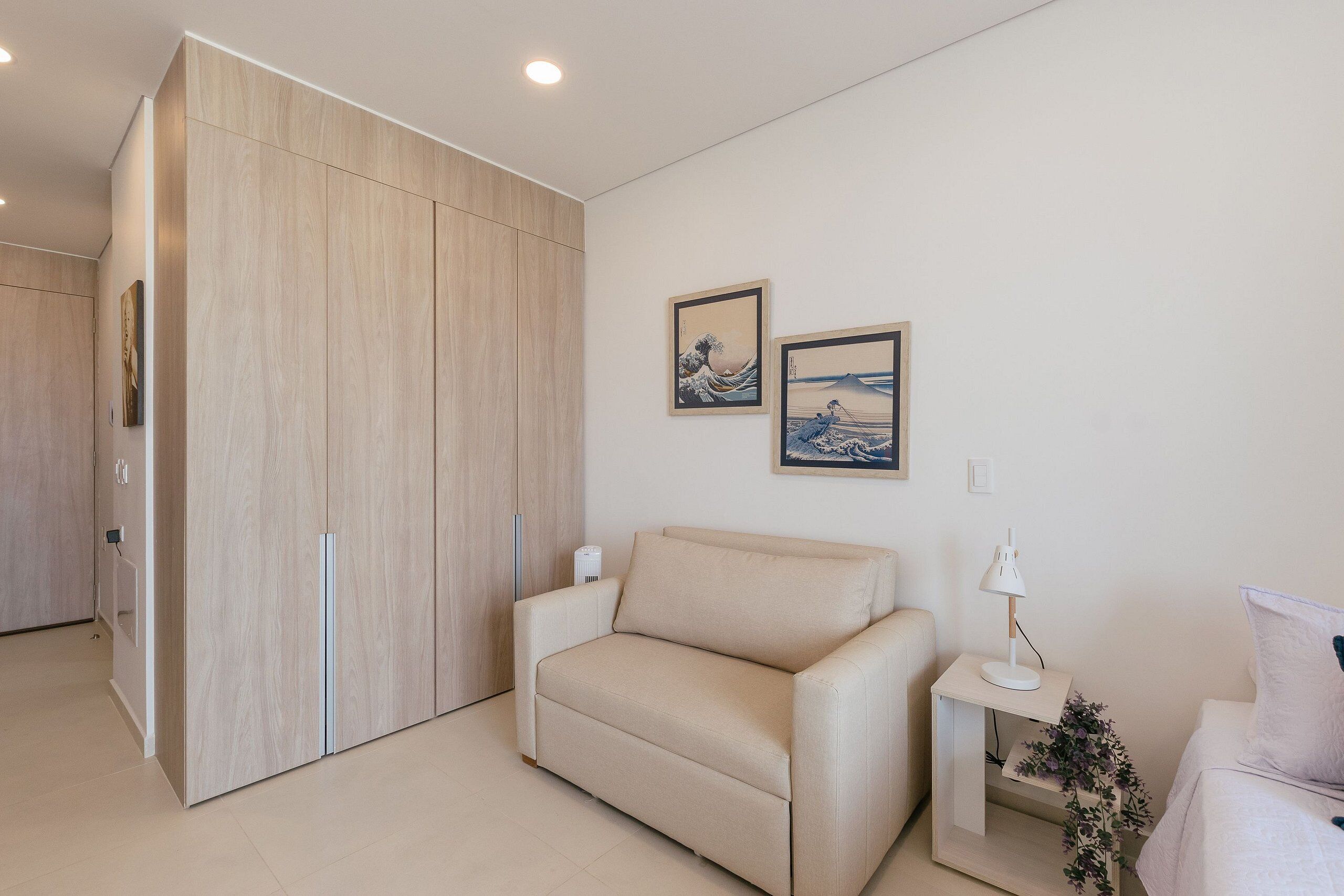 Uma sala de estar moderna com um sofá, uma mesa pequena com um abajur e duas fotografias emolduradas na parede.