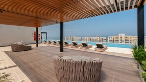 Un salon sur le toit offrant une vue sur la piscine, doté de chaises longues et d’une pergola en bois.