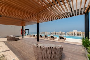 A rooftop lounge with a pool view, lounge chairs, and a wooden pergola. - U-GO Delventto - Pozos Colorados (Santa Marta)