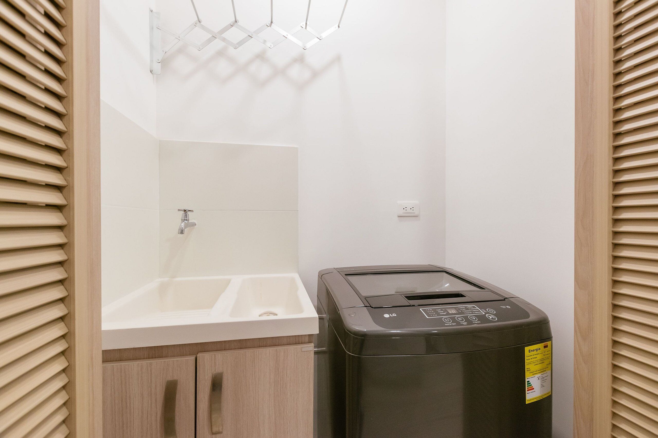 Un baño con lavamanos blanco, un espejo y un cubo de basura negro con etiqueta de eficiencia energética.