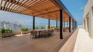 Une terrasse sur le toit agrémentée d’une pergola en bois, d’une table à manger avec des chaises, de plantes en pot et offrant une vue sur la ville.