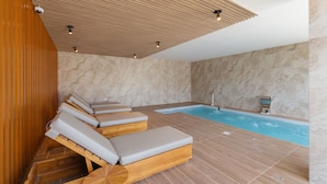 Ein Wellnessbereich mit Holzliegen, einem Whirlpool und einer Steinwand.