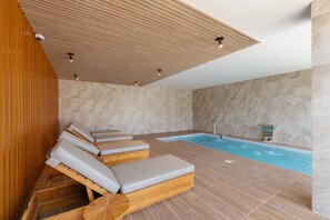 Un espacio de spa con tumbonas de madera, un jacuzzi y una pared de piedra.