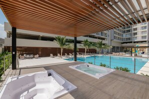 A rooftop pool area with two hot tubs, a wooden pergola, and a view of a building with balconies. - U-GO Delventto - Pozos Colorados (Santa Marta)