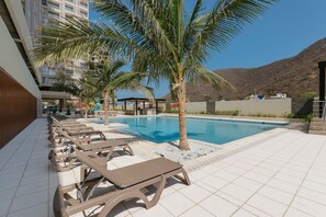 Un espace piscine avec des chaises longues, des palmiers et une vue sur une montagne.