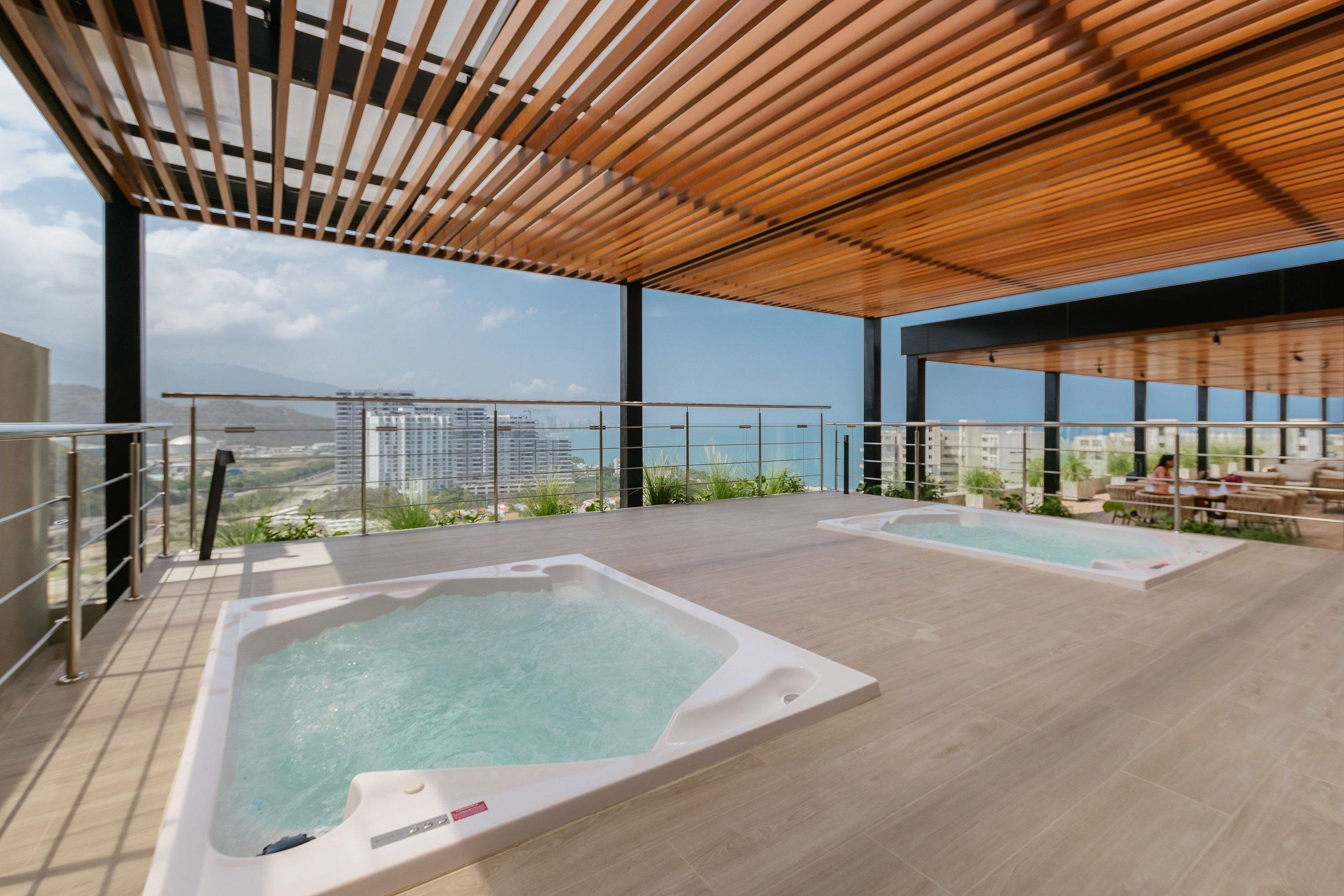 Una terraza en la azotea con dos jacuzzis, una pérgola de madera y vistas panorámicas de la ciudad.
