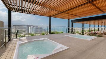 Una terraza en la azotea con dos jacuzzis, una pérgola de madera y vistas panorámicas de la ciudad.