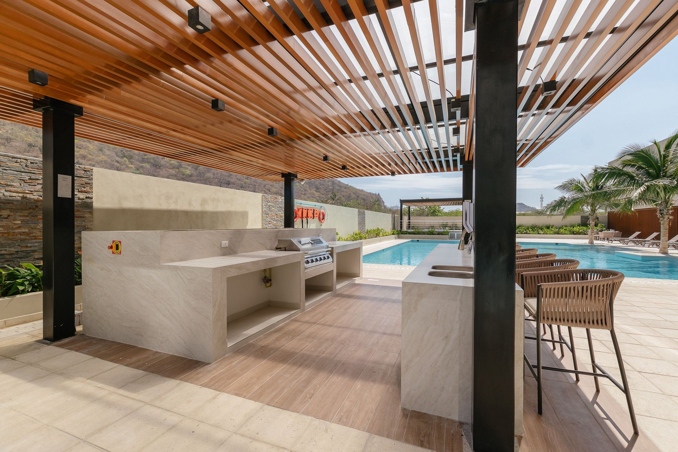 Un patio exterior con una parrilla incorporada, zona de estar y piscina.