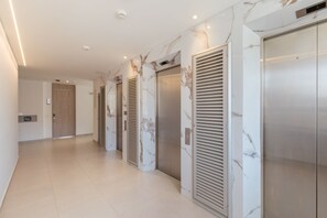 Un pasillo con tres ascensores, paredes de mármol y una puerta al final.