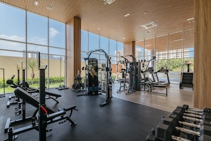 A gym with various exercise equipment, large windows, and a view of buildings outside. - U-GO Delventto - Pozos Colorados (Santa Marta)