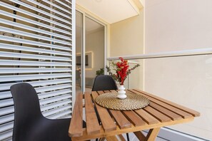 A wooden table with a woven placemat and a vase of red flowers, positioned next to a black chair in a modern room with white blinds. - U-GO Delventto - Pozos Colorados (Santa Marta)