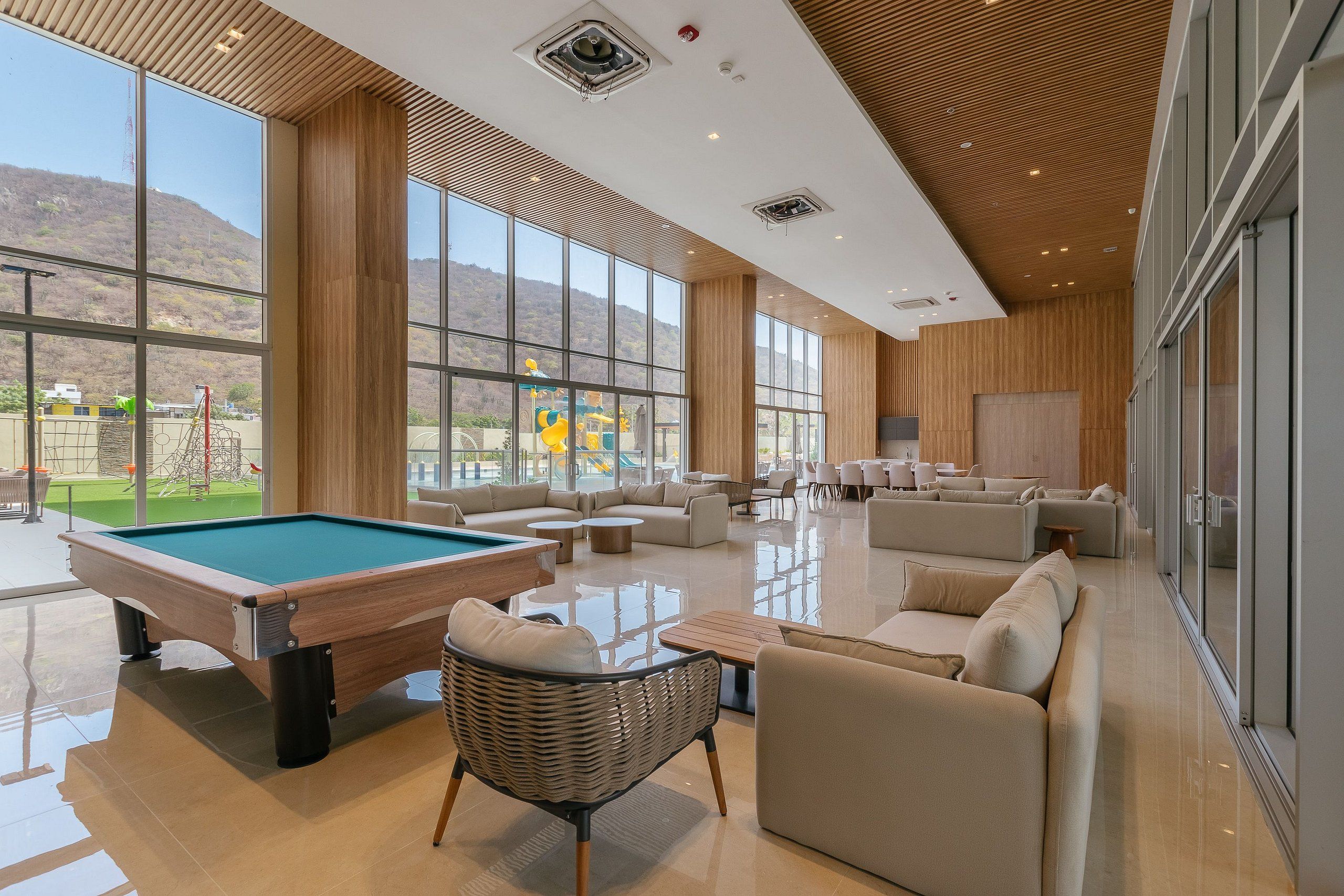 A spacious indoor area with a pool table, comfortable seating, and large windows offering a view of the outdoors.