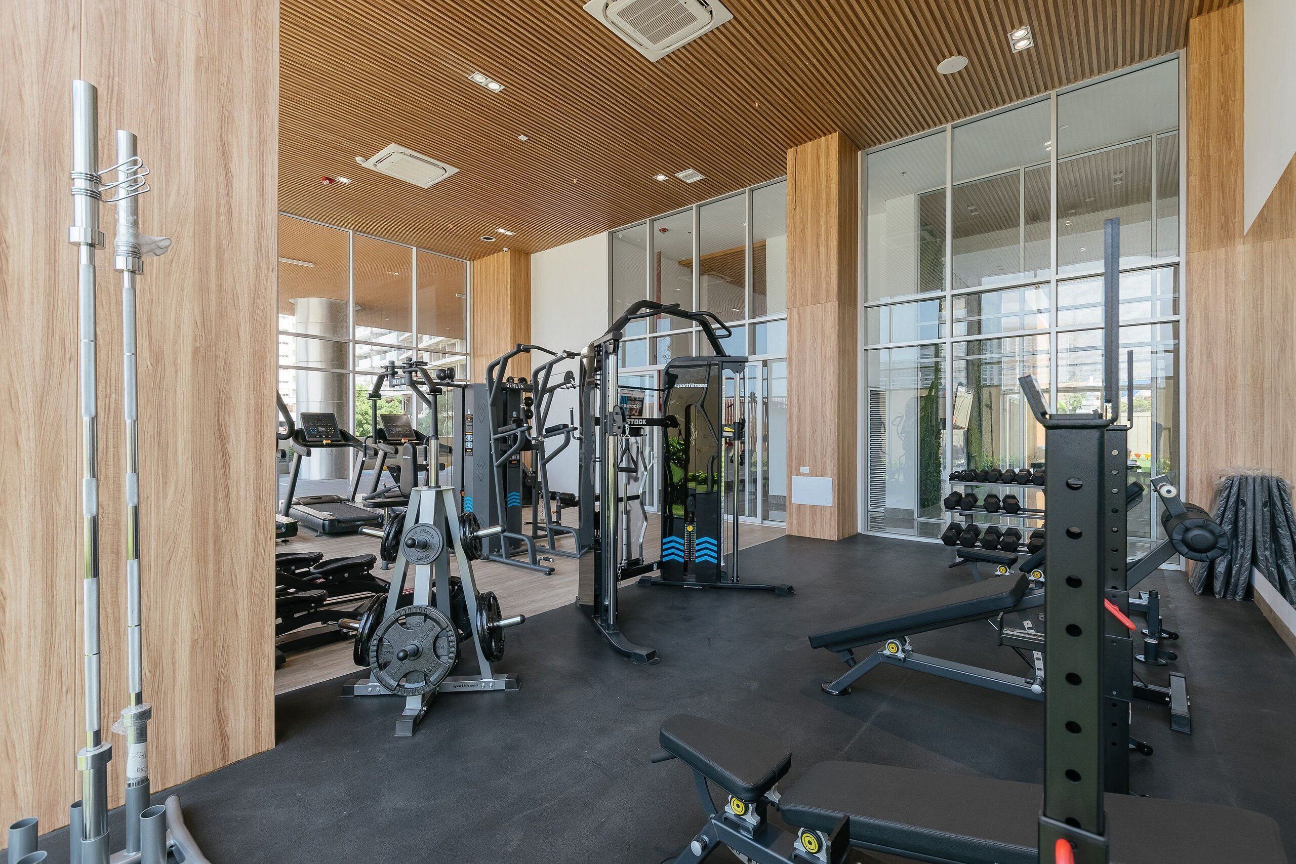 Une salle de sport moderne dotée de divers appareils d’exercice, de grandes fenêtres et d’un plafond en bois.