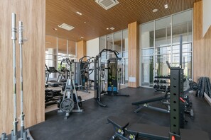 Une salle de sport moderne dotée de divers appareils d’exercice, de grandes fenêtres et d’un plafond en bois.