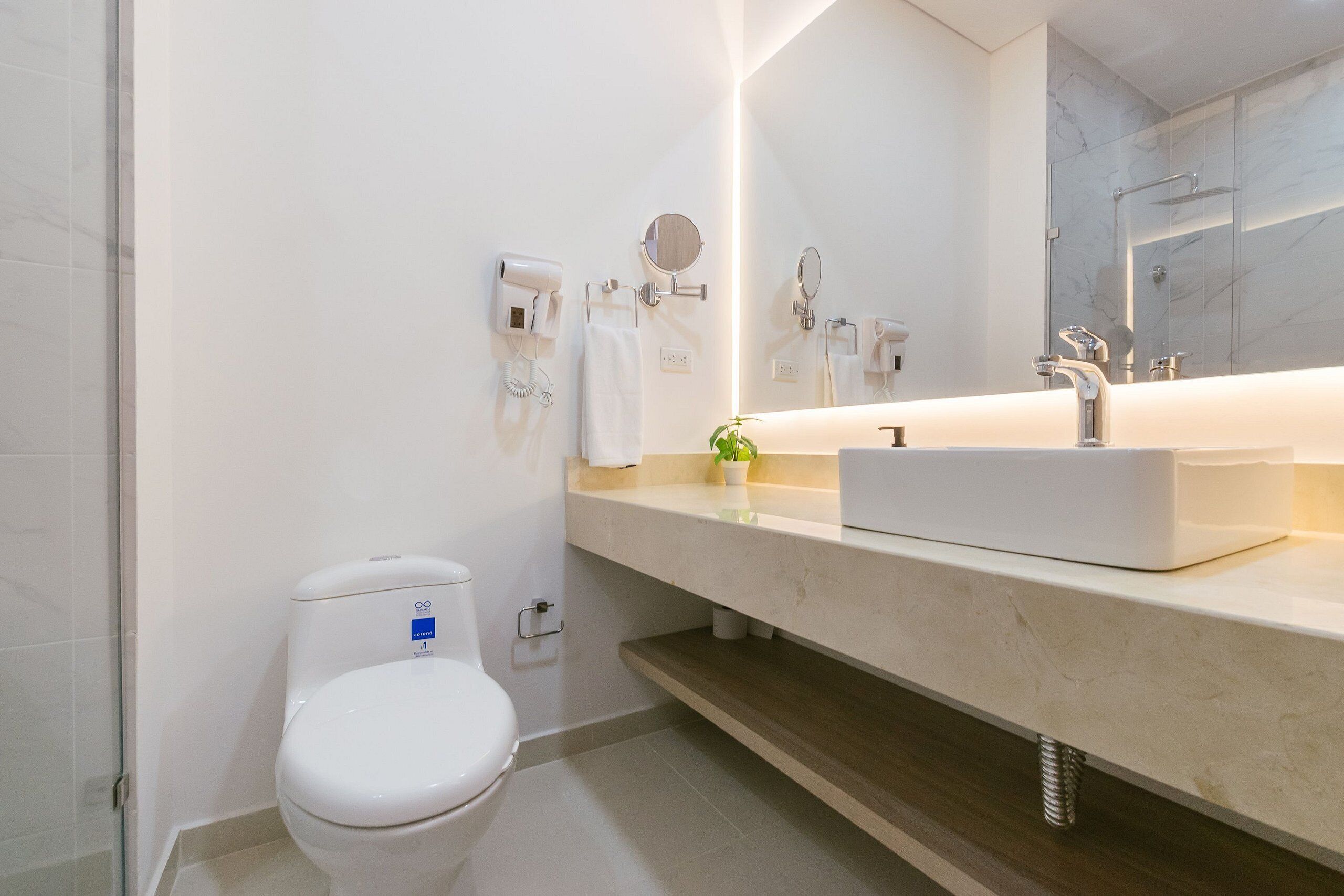 Uma casa de banho moderna com sanita branca, uma pia com espelho em cima e zona de duche com porta de vidro.