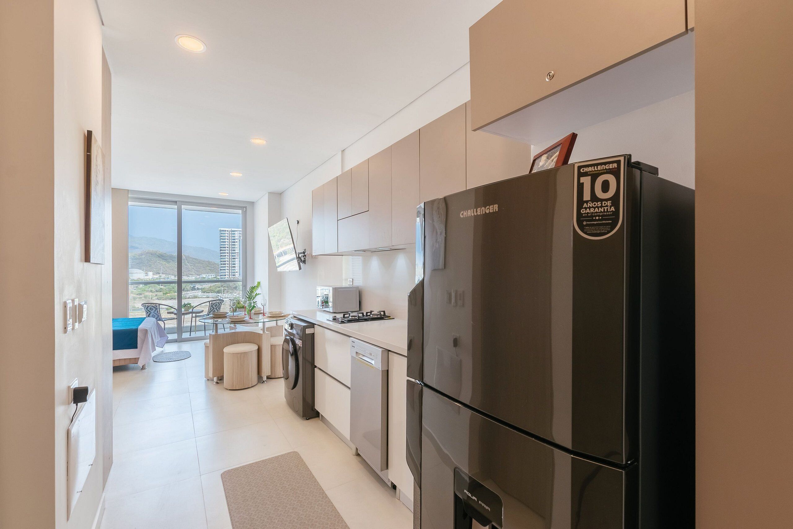 A modern kitchen with a large refrigerator, a dining area with a view, and a small seating space.
