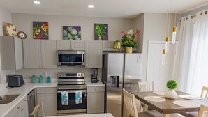Une cuisine moderne avec des meubles blancs, des appareils en acier inoxydable et une table à manger en bois, accompagnée de chaises.