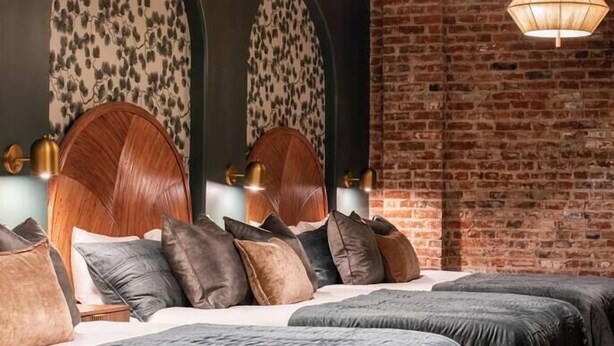 Une chambre moderne avec un mur en briques, deux têtes de lit en bois et trois lampes suspendues.