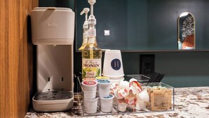 Une petite cuisine équipée d’une machine à café, d’une bouteille de sirop à la vanille française de la marque Monin, ainsi que de divers condiments et ustensiles.