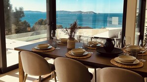 Un coin repas avec vue sur la mer, comprenant une table dressée avec des assiettes, des verres et un vase.