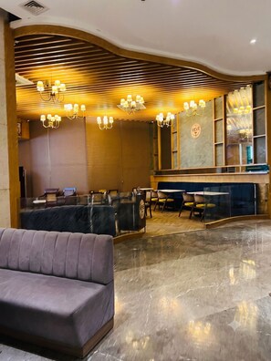 A hotel lobby with a plush sofa, a bar area, and a seating arrangement with tables and chairs. - OnlyStay Villa Vista Supernova (Noida)