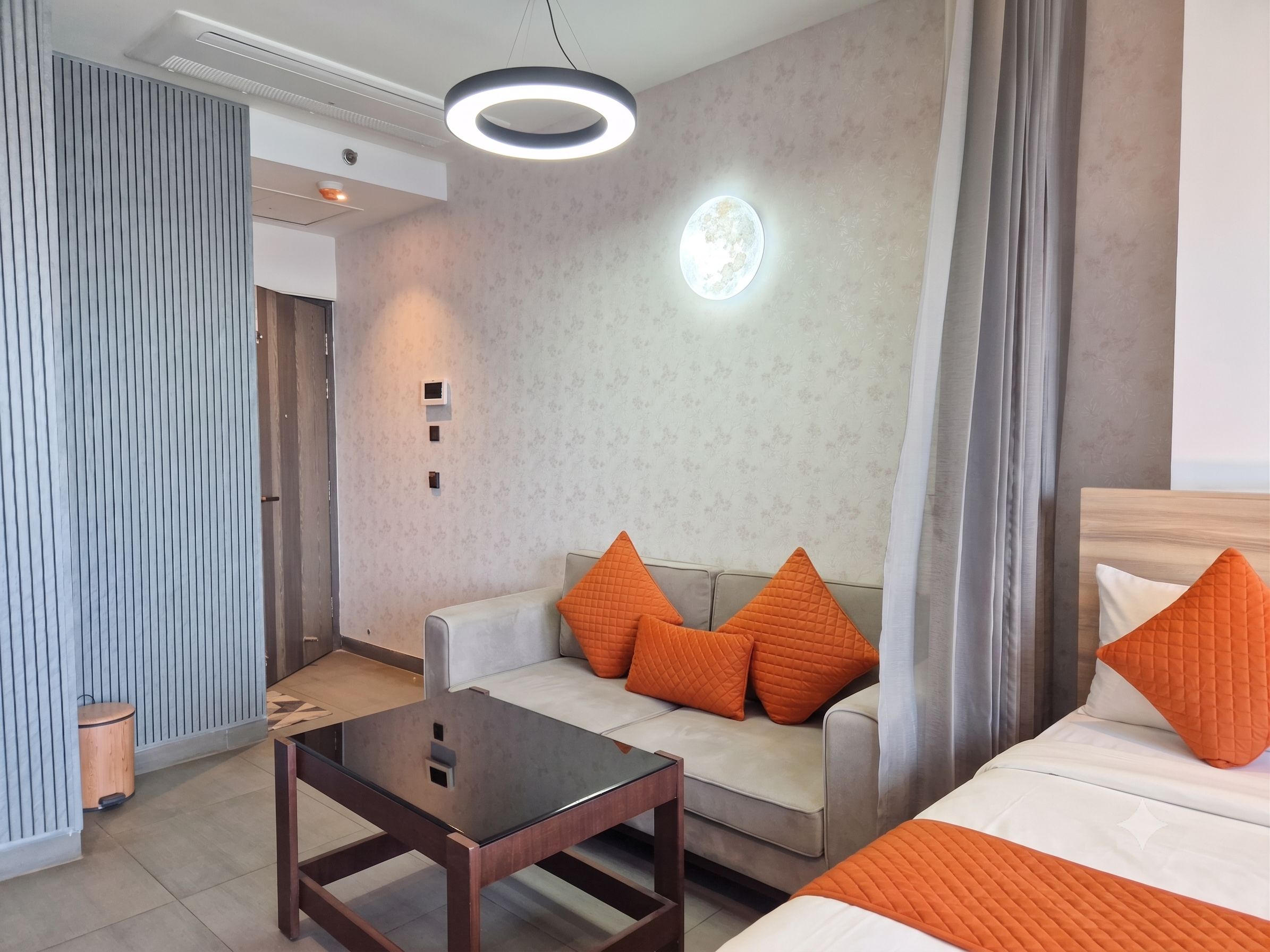 A modern hotel room with a sofa, a bed, a small table, and a unique circular light fixture.