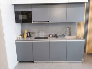 A modern kitchen with grey cabinets, a microwave, a kettle, and a sink. - OnlyStay Villa Vista Supernova (Noida)