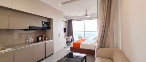 Habitación de hotel moderna con kitchenette, sofá, cama y un amplio ventanal con vistas.